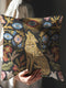 A square decorative throw pillow case with a dark charcoal background and a detailed, faux embroidery design. In the center, a golden-yellow howling wolf sits among colorful botanical flowers and leaves. Above the wolf is a celestial sunburst with a single protective evil eye. The central design is framed by more floral elements and six additional blue evil eye motifs, creating a symmetrical, mystical pattern. This gothic, witchy cushion cover has a distinct dark academia and bohemian aesthetic.